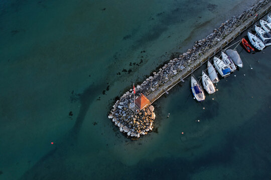Aerial view of a stone pier with a small red-roofed hut and sailboats docked in the clear turquoise waters of Lake Geneva Morges, Vaud, Switzerland.