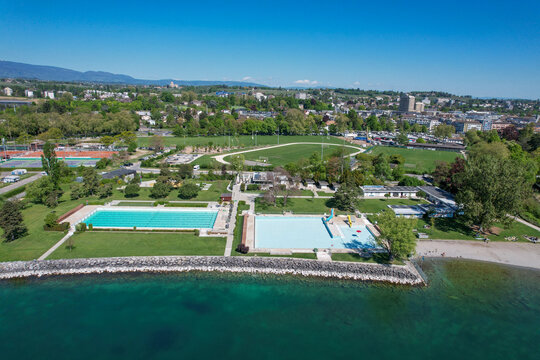 Aerial view of the public swimming pool complex and sports facilities along the shores of Lake Geneva with green lawns and athletic tracks in Morges, Vaud, Switzerland.