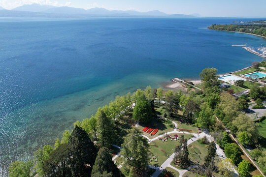 Aerial view of the lush Parc de l'Independance with colorful flower beds and green trees along the shores of Lake Geneva with mountains in the background in Morges, Vaud, Switzerland.