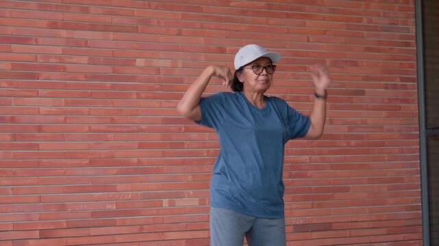 A senior woman stays active and energetic by exercising through aerobic dance. Positive emotion reflects a healthy lifestyle, embracing movement and workout routines to strong in her elderly years