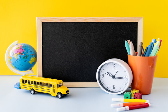 School admin core time blocking study setup with blank chalkboard, globe, clock, toy school bus and dopamine stationery, global classroom edutainment vibe in bright yellow and blue desk still life