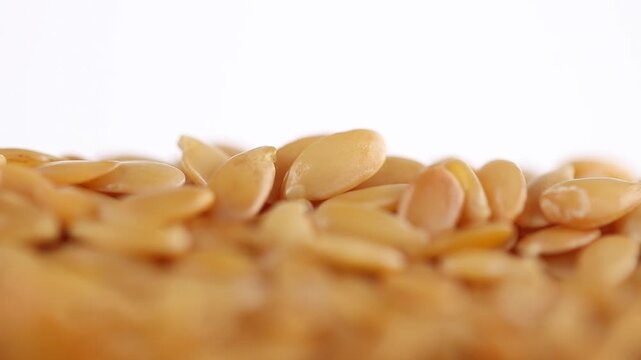 Plie of golden raw flax seeds rotating on a white background. Close-up