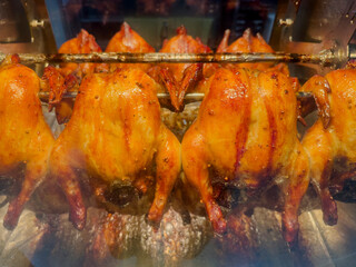 Naklejka premium Golden brown rotisserie chickens cooking on a spit in a professional roaster oven, juicy roasted poultry, street food market style.
