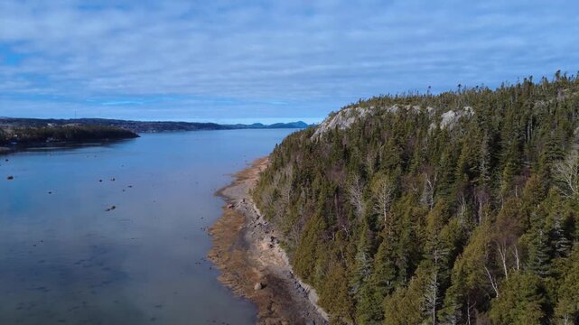 High-resolution drone shot over the St. Lawrence River between &Icirc;let Canuel and Rimouski, capturing moody clouds and the rugged horizon of Bic National Park, Quebec.