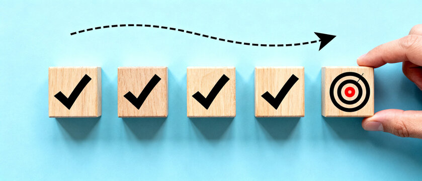 Achieving business goals by completing tasks in a strategic and organized manner, represented by wooden blocks with checkmarks and a bullseye