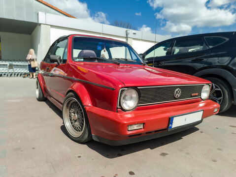 Polska, Ostrowiec Świętokrzyski, 23 kwietnia 2026, 12:34. Czerwony kabriolet Volkswagen Golf na parkingu w wiosenny dzień. Samoch&oacute;d charakteryzuje się klasycznym designem z okrągłymi reflektorami.