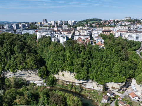 Aerial view of the Sarine river winding through steep sandstone cliffs and dense green forests below the historic city skyline Fribourg, Fribourg, Switzerland.