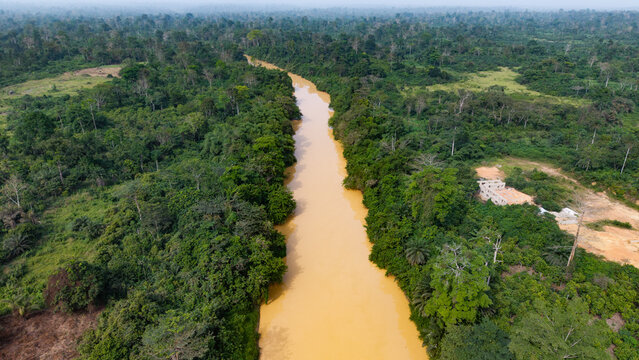 Brown, muddy river flowing through a deforested landscape, showing environmental destruction from illegal mining