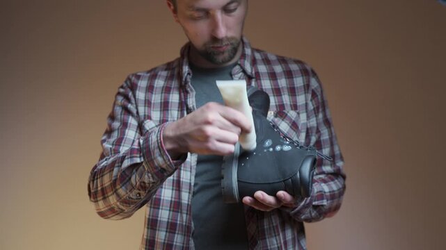 Shoe care in action as cream is applied to black leather boot. Man applies leather cream to black boot, detailed shoe care and maintenance. Leather boot maintenance in progress as cream is applied