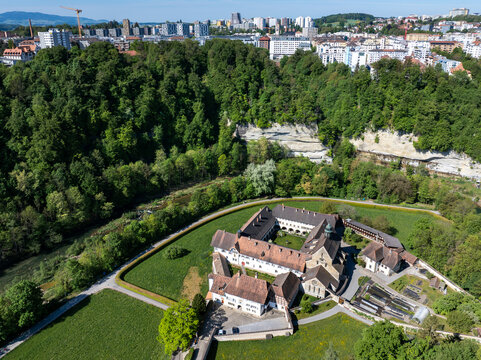 Aerial view of the historic La Maigrauge abbey complex nestled among lush green forests and the Sarine river with the city skyline in the background in Fribourg, Fribourg, Switzerland.