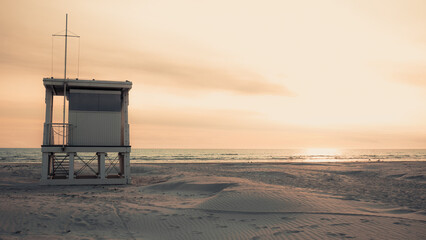 Guarding the shoreline-solitary lifeguard tower stands on empty Baltic beach in Liepaja, framed by open horizon and soft evening light. Solitude and seasonal coastal atmosphere with copy space © Nimbus Works
