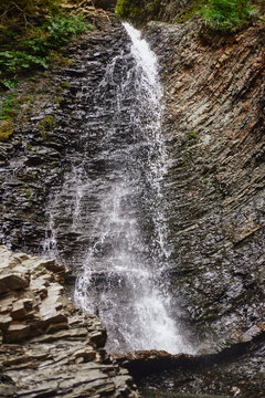 Zhenetskyi Huk Waterfall. Water flows down a rocky cliff in a forested area during midday. Summer Hiking in Carpathian Mountains. Ukraine