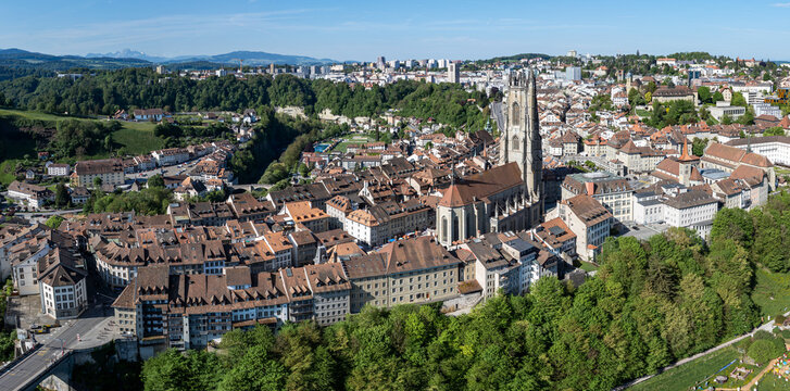 Aerial view of St-Nicolas Cathedral surrounded by historic rooftops and lush green trees in Fribourg, Fribourg, Switzerland.