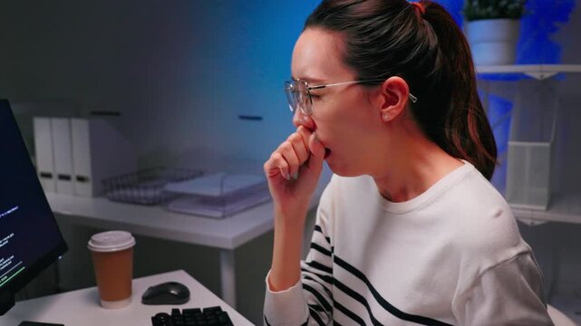 Focused Asian female programmer working overtime at night while coding on computer in modern office. Software development, deadline pressure, startup culture and women in tech concept.