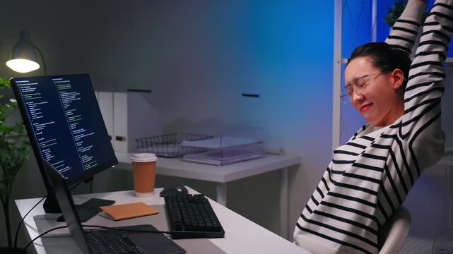 Focused Asian female programmer working overtime at night while coding on computer in modern office. Software development, deadline pressure, startup culture and women in tech concept.