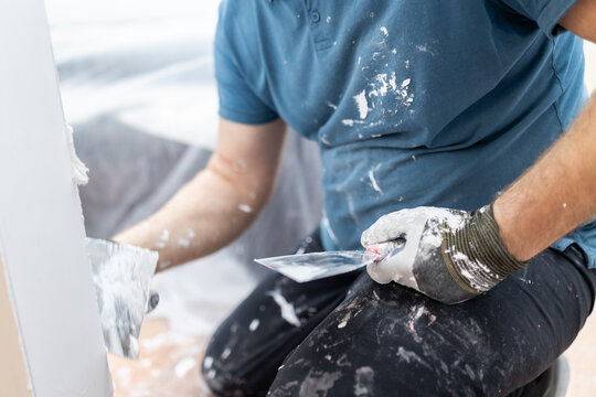 Close Up of Plasterer Holding Putty Knives During Wall Repair