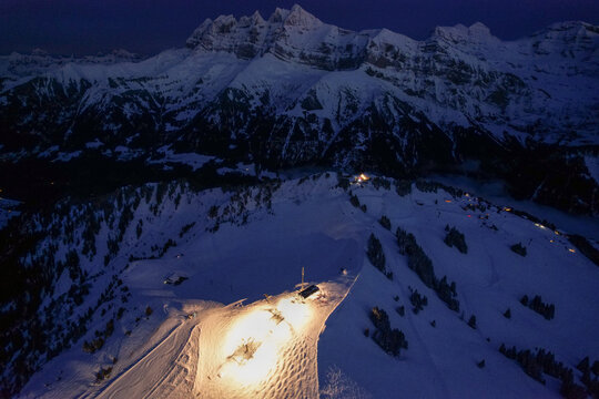 Aerial view of Les Crosets ski resort and the Dents du Midi mountain range under a twilight sky with illuminated slopes in Val-d'Illiez, Valais, Switzerland.
