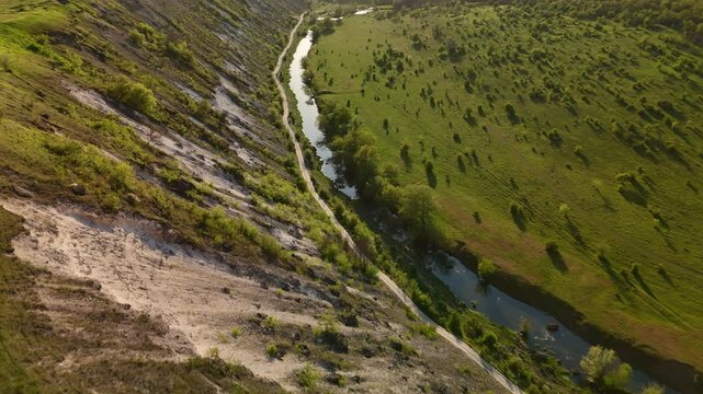 Aerial River Winding Through Green Valley, Cinematic Drone Sweep Over Golden Hillside Slope And Reflective