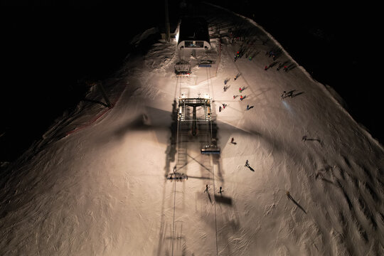 Aerial view of Les Crosets ski resort at night with an illuminated chairlift station and skiers on the snow in Val-d'Illiez, Valais, Switzerland.