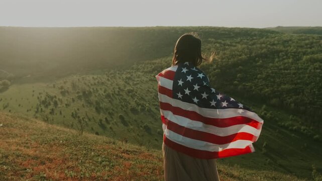 Woman In Flag Observes Valley At Dusk. Woman Draped In American Flag Views Sunset Over Peaceful Valley