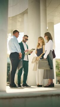 Four business people meet outdoors, discussing documents and charts together. They are collaborating on a project, showcasing teamwork and professional communication.