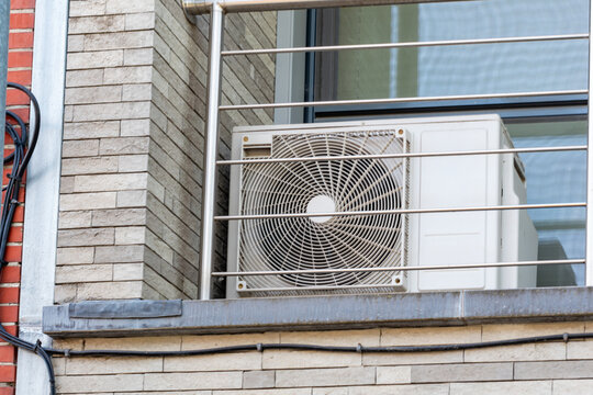 Outdoor air conditioner unit installed on a modern apartment balcony. External split system air conditioning compressor on a building facade with brick wall.Air conditioning system outdoor unit mounte