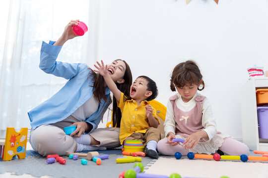 Asian teacher and diverse children playing with colorful educational toys in a bright nursery room
