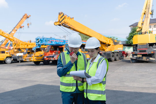 Engineers use a radio and checklist during crane inspection in a heavy equipment yard, coordinating safety, maintenance tasks, and lifting operation readiness at work.