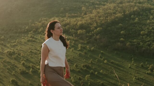 White Woman Walking Hilltop At Sunset, Traveler Pausing To Gaze Over Green Valley, Flowing Skirt Catching Warm