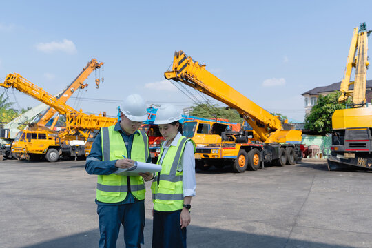 Engineers in hard hats complete a crane inspection checklist at a heavy equipment yard, supporting safety, maintenance planning, and industrial lifting readiness.