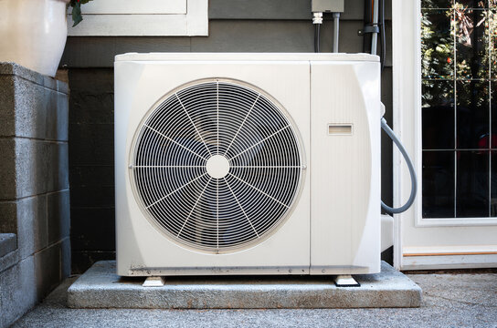 Heat pump outside of home. All-electric HVAC system for heating and cooling with thermal energy transfer. Modern high efficiency heating system on concrete slab. Vancouver, BC. Selective focus.