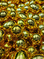 A dazzling array of shiny gold capsules reflects the rhythmic light of the ceiling lights, creating a surreal metallic tapestry of distorted luminosity. Gold gradient background. Vending machine © Robert Yap