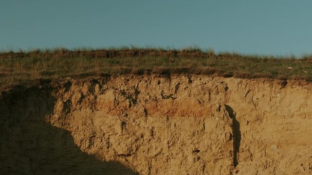 Eroded Cliff Face With Exposed Strata And Rugged Texture, Sunlit Shadows Carve The Bluff, Dry Soil And Layered