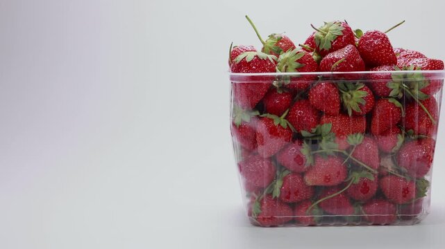 Tracking right across fresh red strawberries in plastic container on white background