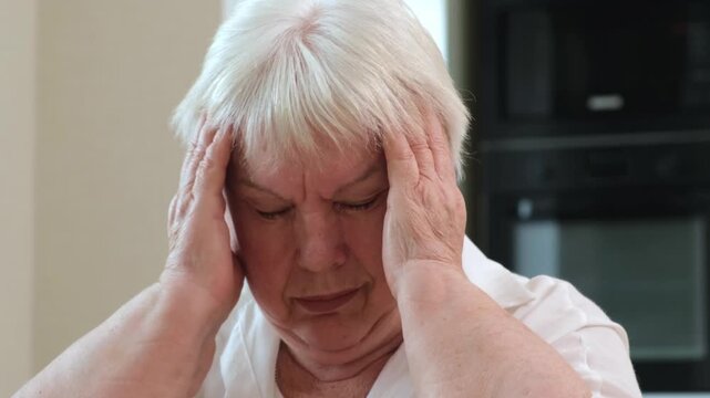 Elderly woman suffering from severe headache rubbing temples with closed eyes close up. Concept of migraine, high blood pressure and health problems