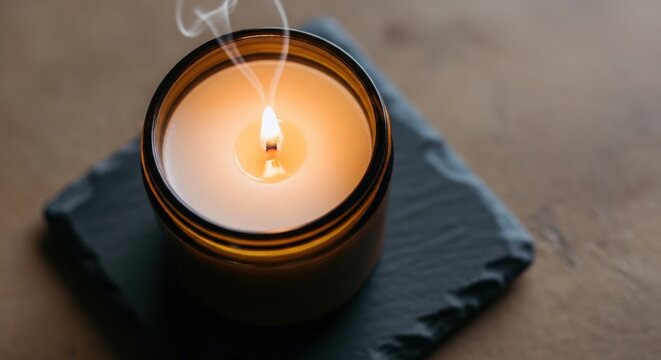 Close-up of a lit soy wax candle with a natural cotton wick burning in an amber glass jar, casting a warm glow.