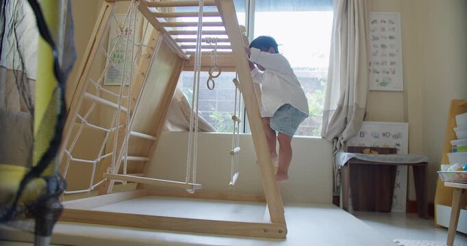 A curious toddler climbs a wooden indoor gym, developing gross motor skills and independence during active play in a Montessori-style learning environment.