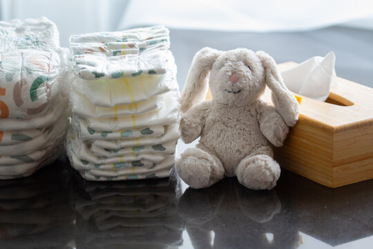 Stack of diapers with a toy bunny and a box of napkins on the table. Newborn nappies concept, highlighting baby products, diaper promotions, or child care