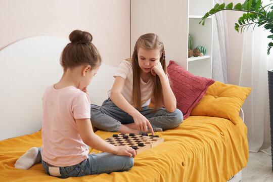Two sisters playing checkers on a bad having fun at home, happy children concept