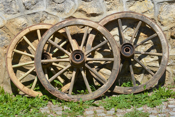 Obraz premium Three weathered wooden carriage wheels leaning against a rustic stone wall on a sunny day in a traditional courtyard