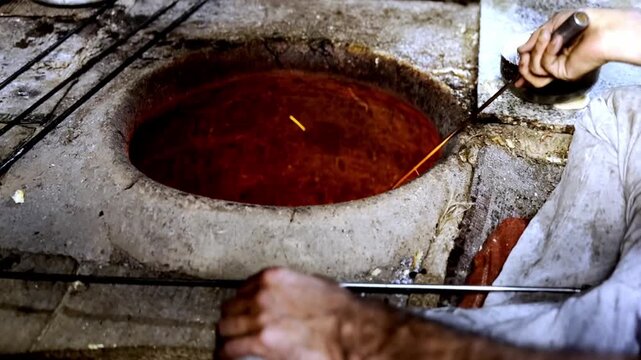 Making bread in traditional clay tandoor oven using wood fire, rural cooking method preparing fresh flatbread in village kitchen