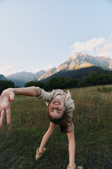 Naklejka premium Woman outdoors in a meadow with mountains in the background performs a dynamic backbend, exuding playful energy, balance, and a joyful mood in a natural setting.