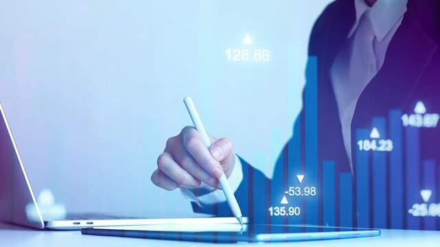 Business person analyzes data on digital tablet while using laptop in office on a weekday morning.