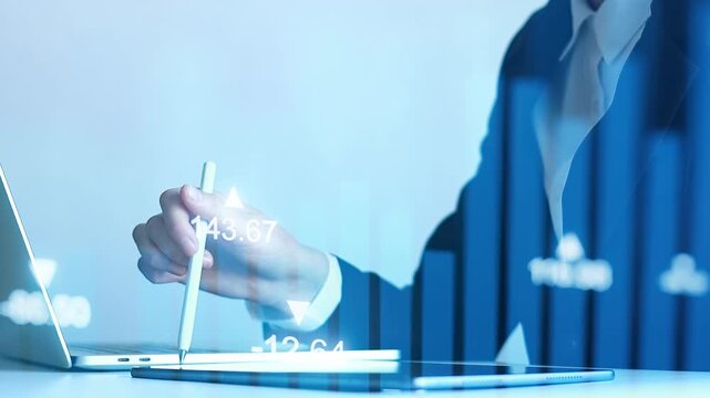 Business person analyzes financial data with laptop and tablet in office setting during daytime.
