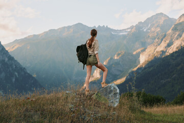 Naklejka premium Woman hiking outdoors with backpack in a mountain landscape, capturing a sense of adventure, balance, and nature in a sunlit breeze and expansive scenery