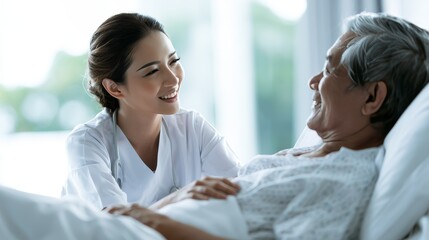 Fototapeta premium Smiling Asian Nurse Comforting Elderly Patient in Hospital Bed