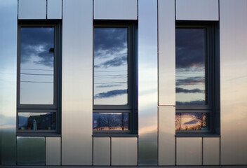 Fototapeta premium unset sky reflected in three windows of a modern office building, warm tones and clean lines creating a minimal urban composition with soft evening light.