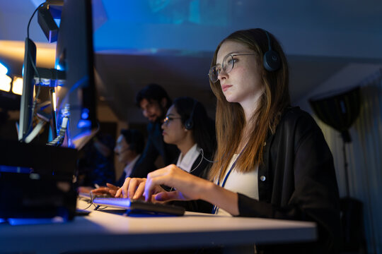Young female customer service operator wearing headset working on computer in office. Professional woman developer support project in modern coworking space at night