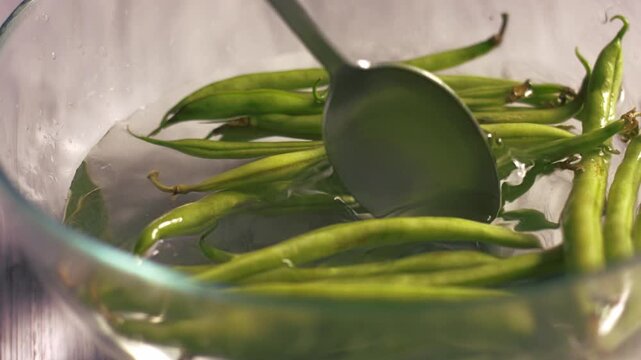 Stirring raw green beans floating in bowl of water