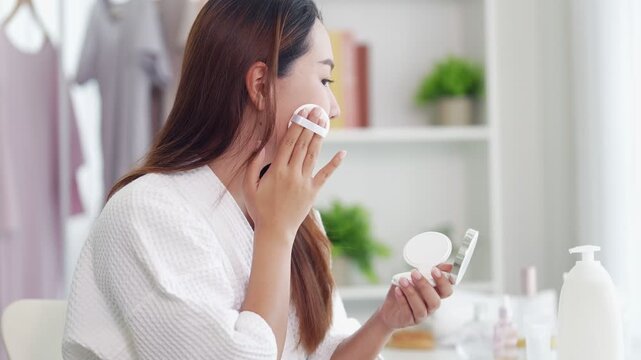 young Asian women applying foundation makeup using cosmetic sponge puff for facial beauty skincare morning routine in bathroom home preparing for work day